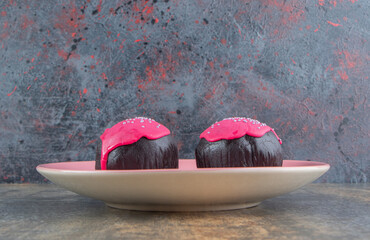 Two sweet chocolate doughnuts with pink frosting and sprinkles