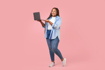 Wall Mural - Cheerful Black Overweight Freelancer Lady Using Laptop Over Pink Background