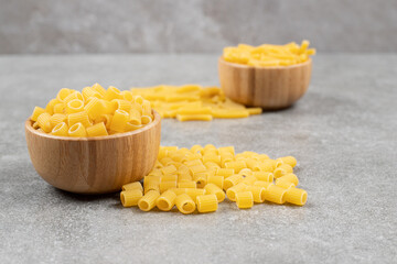 Two bowls of raw macaroni on marble surface