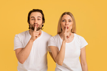 Happy young caucasian couple in white t-shirts make secret gesture, take fingers to lips