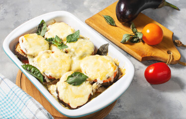 Eggplant baked with mozzarella cheese, tomatoes in baking dish on concrete table. Vegetarian food recipe