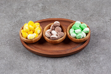 Wall Mural - Bowls of colorful candies on wooden plate