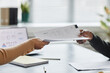 © Seventyfour - Close up of two hands handing document or contract over meeting table in office