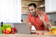 © Prostock-studio - Glad millennial african american man at table with organic vegetables uses laptop, waving hand for video call