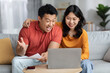 Happy asian spouses reading papers, using laptop at home