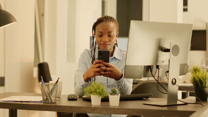 Poster - portrait of startup employee using smartphone at office job during sunset, working on business data 
