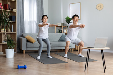 Happy asian couple having morning workout at home, using laptop