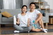 Active asian spouses exercising together at home, drinking water