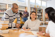 © JackF - Group of positive adult hispanic students communicating in library, talking, reading books and making notes