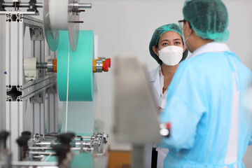 Wall Mural - Inspector woman and colleague man working on quality of mask and medical face mask production line, Industry and factory concept.