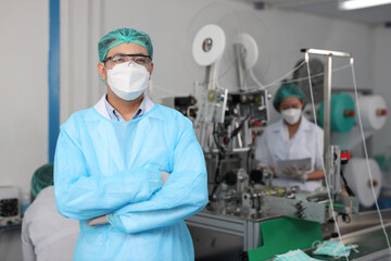 Canvas Print - Worker in personal protective equipment or PPE inspection quality crossed arms and looking camera in mask and medical face mask production line factory, manufacturing industry and factory concept.