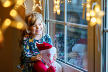 Little Preschool Girl Holding Cup Santa Claus Boot With Gift Called Nikolausstiefel In German. Happy Child Wait On Holiday By Window With Christmas Lights In Winter. Cozy Family Celebration Of Xmas.