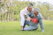 © feeling lucky - Asian senior man standing and suffering from chest pain or heart attack from walking accident in garden outdoor. Elderly woman caregiver consoling and help him while hugging support. First aid concept