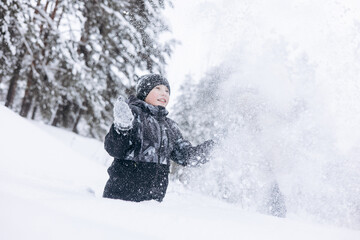 Wall Mural - Happy teenager boy sitting on snow in winter forest. Child having fun outdoors. Joyful adolescent playing in snow at snowfall. Laughing smiling kid walking in winter park in cold weather