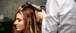 The female hairdresser is curling hair for a brown-haired young caucasian woman in a beauty salon