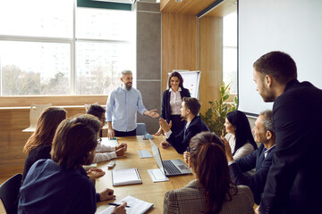 Wall Mural - Middle-aged grey-haired businessman make presentation for diverse businesspeople in boardroom. Successful business trainers lead meeting with employees in office. Teamwork and leadership.