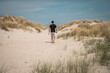 Young man (guy) going for a walk in the dunes and sand beach on the Northsea coast of the german island Juist. Blue clouded sky and bushes of grass. Perfect summer trip.