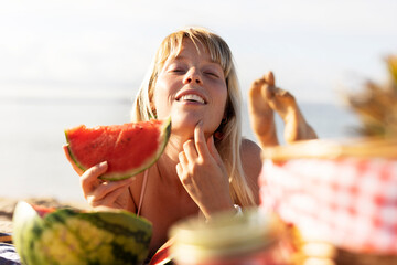 Wall Mural - Cheerful young woman enjoy at tropical sand beach. Portrait of happy girl with fruit. Young woman having a picnic on the beach