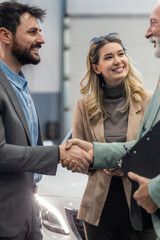 Young couple looking to buy a new car. Car salesman making a sale. Signing a papers for purchase a new car