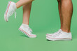 © ViDi Studio - Cropped close up side view photo shot caucasian young couple two friends family man woman wear basic sneakers shoes together stand on toes isolated on pastel plain light green color background studio.