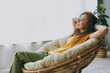 © ViDi Studio - Side view fun young woman of African American ethnicity 20s wear casual clothes sits near window in armchair close eyes dream stay at home flat rest relax spend free spare time in living room indoor