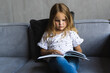 © F8  \ Suport Ukraine - Cute little small girl reading book on sofa at home