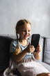 © F8  \ Suport Ukraine - Portrait of cute little cute girl holding smartphone and resting at sofa at home. Choosing favorite music or cartoons,texting messages, browsing internet, watching video, playing games onphone