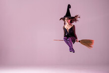 A Ballerina On Pointe Shoes In A Black Witch Costume In A Hat Flies On A Broomstick On A Lilac Background. Ballet For Halloween. Copyspace.
