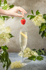 Wall Mural - Real woman preparing Elder Fashion Royal Cocktail in Champagne glass surrounded by ingredients and bar tools on gray table surface