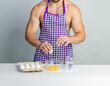 © oleg_ermak - Chef bodybuilder in protective apron and cook eggs on whie kitchen table. Muscular man cooking. Healthy food and dieting. Food additives for sportsman, daily calorie diet