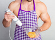 © oleg_ermak - Chef bodybuilder in protective apron uses a blender to beat scrambled eggs on whie kitchen table. Muscular man cooking.