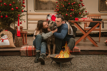 Happy couple in love and their dog spend time together on Christmas holidays. Cane Corso and his owners are celebrating the new year in the open air near the motor home and the fire.