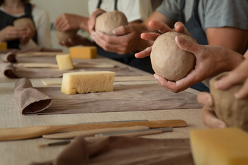 Hands of group of people sculpling mugs from wet clay in pottery workshop