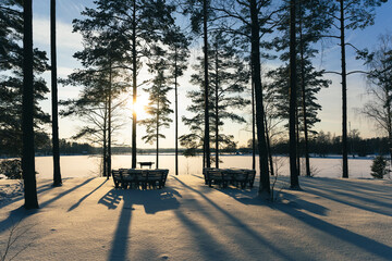 Sticker - Picnic table by the lake under snow in winter. A thick layer of snow after a snowfall covered benches and tables. Pine forest on a sunny winter day. Latvia