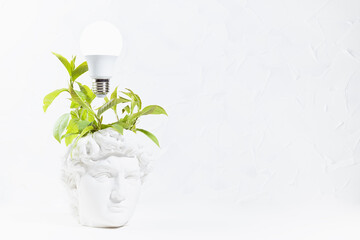 Brainstorming concept - fresh green wreath of leaves as thoughts and glow light bulb over head of white antique statue David in intense thinking and creativity process. College and school education.