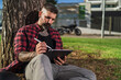 Chico joven tatuado con barba dibujando en tablet digital con su motocicleta de fondo