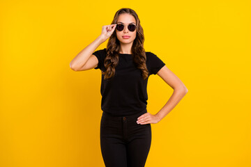 Wall Mural - Photo of serious confident young woman wear black outfit arm dark eyeglasses isolated yellow color background