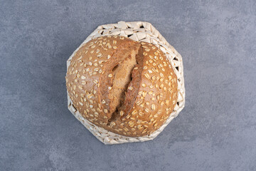 Coating of flakes on a loaf of bread on an upside-down basket on marble background