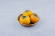 A wicker bowl of three persimmons on white background
