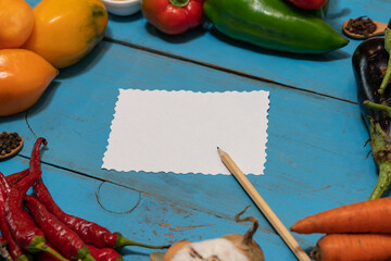 Vegetables are laid out around a sheet of paper and a pencil. Empty space for text. Vegetables, empty blank for recipe on a blue background.