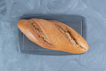 Wall Mural - Navy wooden board under a single loaf of bread on marble background