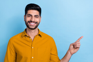 Wall Mural - Photo of cheerful positive beaming toothy man wear yellow shirt smiling indicating at empty space isolated on blue color background