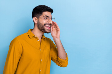 Wall Mural - Photo of funny young handsome man dressed yellow shirt shouting open mouth palm near cheek call someone isolated on blue color background