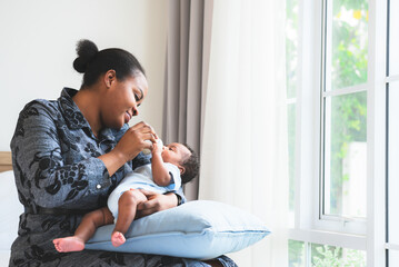 Wall Mural - an African mother feeding milk from bottle milk to her 2-month-old baby newborn son, to African family and food for infant concept.