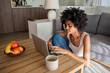 © KAMPUS - Focused businesswoman sitting on floor and typing on laptop. African American copywriter looking at keyboard, chatting with colleague online during self-isolation. Home office, pandemic concept