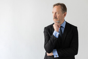 Portrait of pensive mature manager thinking and looking away. Senior Caucasian businessman wearing three piece suit standing with thoughtful expression. Business plans concept