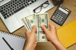 © Oleksandr - Dollar banknotes of money in hands, calculator and laptop over the table. Financial Accounting.