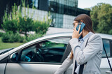 Fototapeta  - Business woman getting into the car and using smartphone