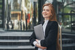 Confident businesswoman model holding laptop looking at camera smiling toothy standing outside outdoor near company. Caucasian female business person on city