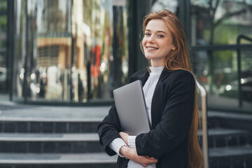 confident businesswoman model holding laptop looking at camera smiling toothy standing outside outdo